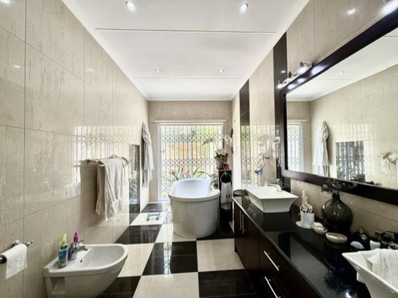 Modern bathroom featuring a freestanding bathtub, wall-mounted bidet, double vanity with vessel sinks, and high-contrast tiled flooring with recessed lighting.