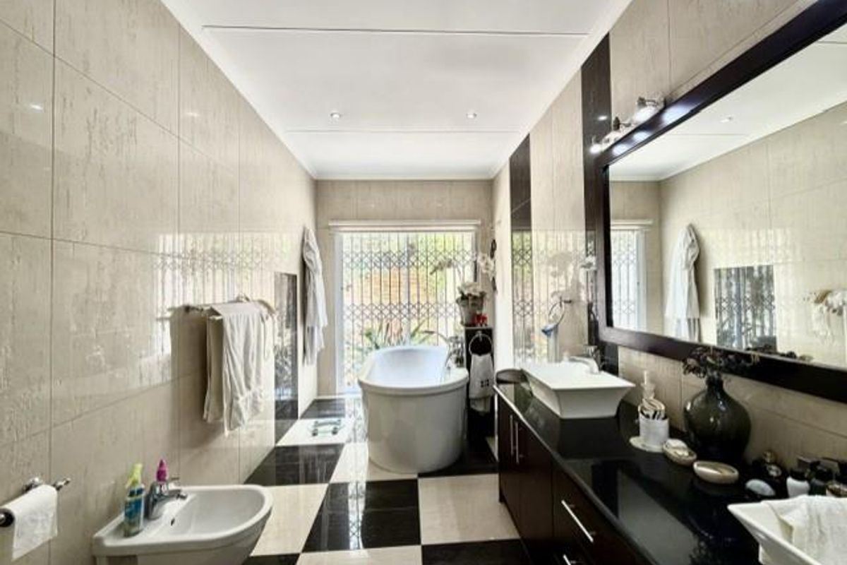 Modern bathroom featuring a freestanding bathtub, wall-mounted bidet, double vanity with vessel sinks, and high-contrast tiled flooring with recessed lighting.