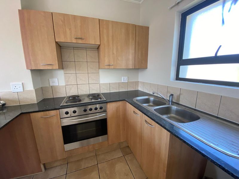 A functional kitchen featuring light wood-finish cabinetry, dark granite countertops, a stainless steel double sink, and a built-in oven with an electric hob.
