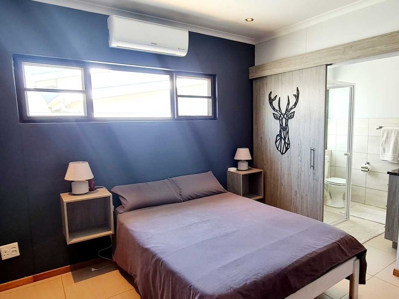 Modern bedroom featuring built-in cupboards, tiled flooring, a split-system air conditioner, and an adjoining en-suite bathroom.