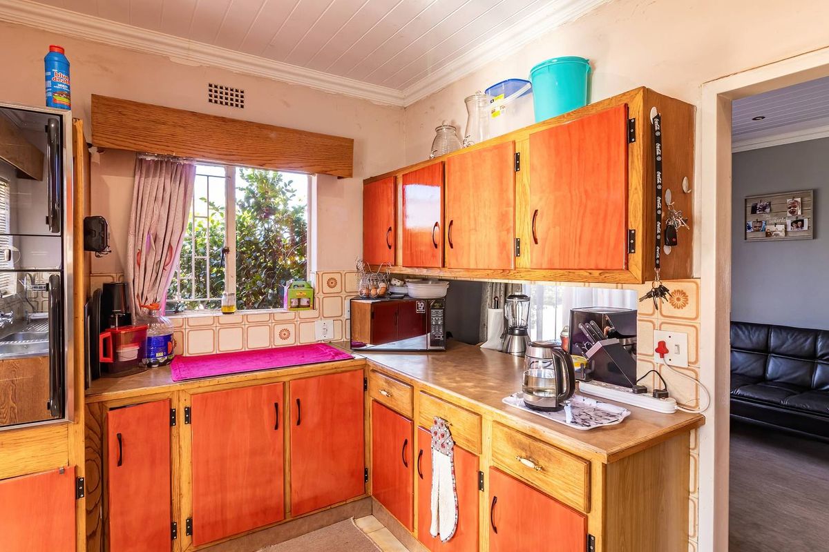 A dated kitchen featuring wooden cabinetry, laminate countertops, and patterned wall tiles, with a window providing natural light and a view of the garden.