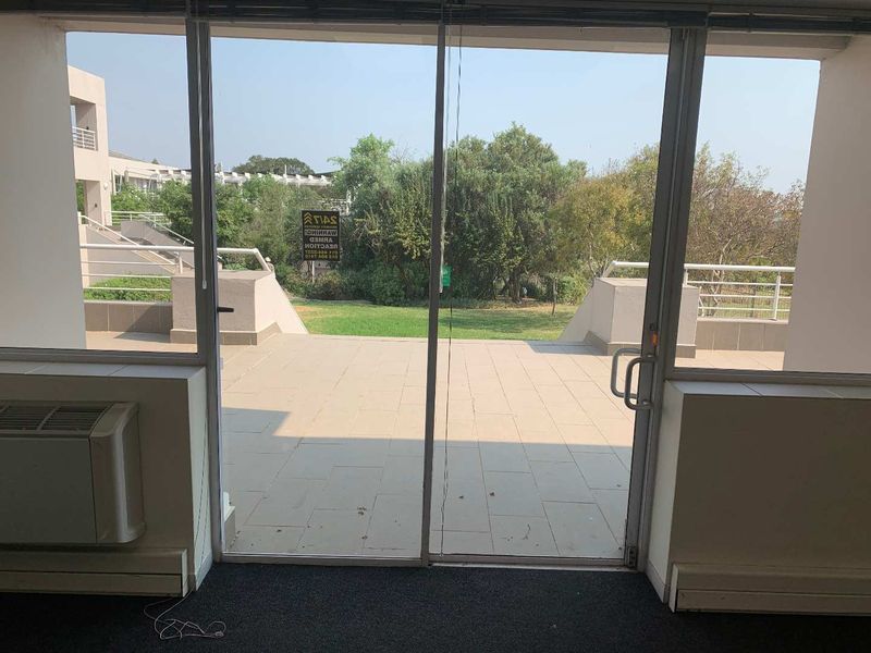 Office space featuring large glass sliding doors opening onto a paved patio area with garden views and integrated HVAC unit.