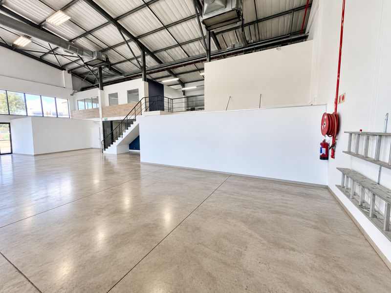Spacious industrial utility area featuring polished concrete floors, exposed steel roof structure, mezzanine level with staircase, and integrated fire safety equipment.