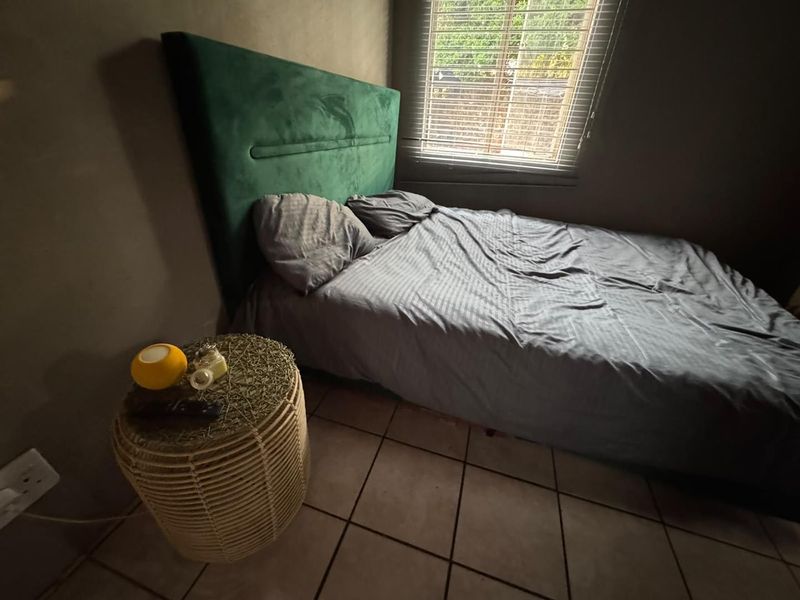 A bedroom featuring tiled flooring and venetian blinds, providing a functional space with neutral wall tones.