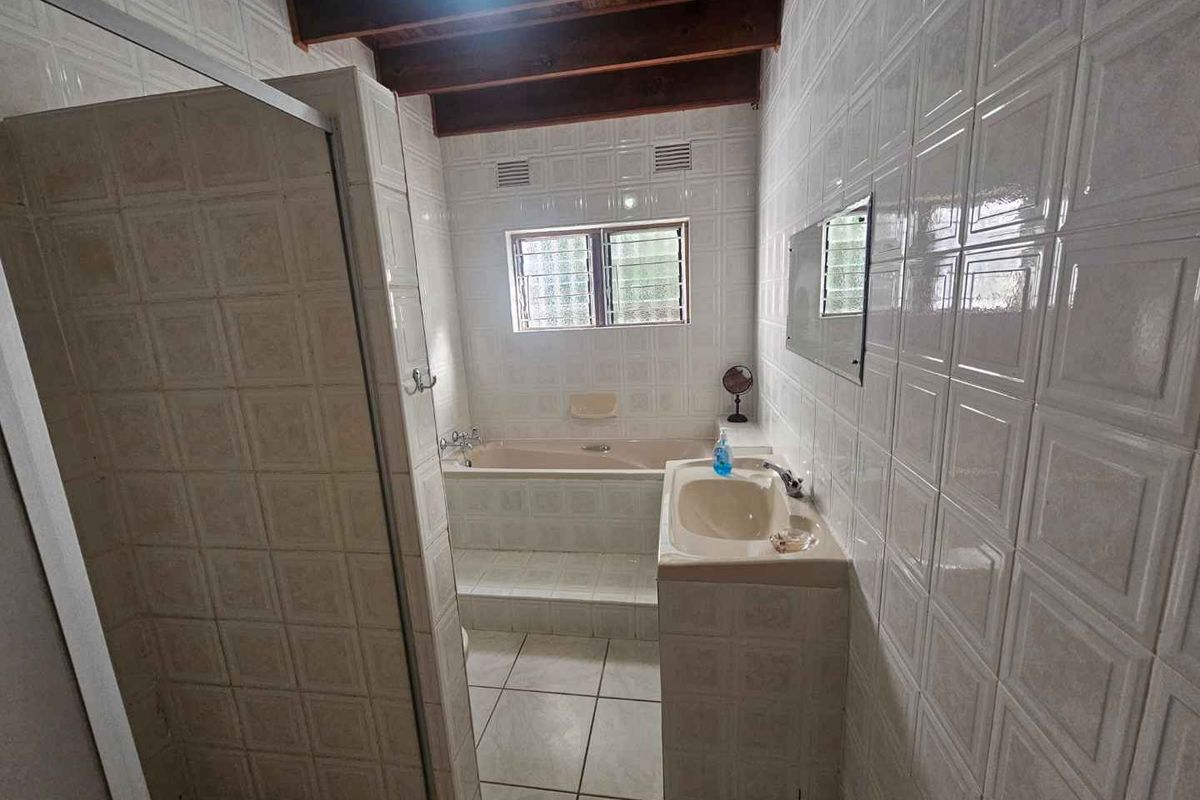 A functional bathroom featuring a built-in bathtub, a pedestal sink, a shower enclosure, and exposed timber ceiling beams.