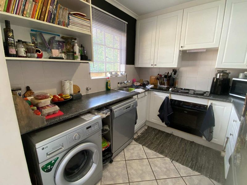 A functional kitchen featuring white cabinetry, dark laminate countertops, tiled flooring, and integrated appliances including an oven and hob.