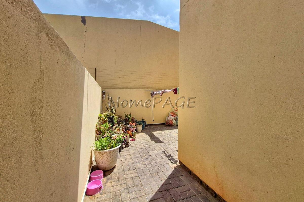 A narrow outdoor courtyard or side passage featuring paved flooring and high boundary walls, requiring maintenance to the wall surfaces.