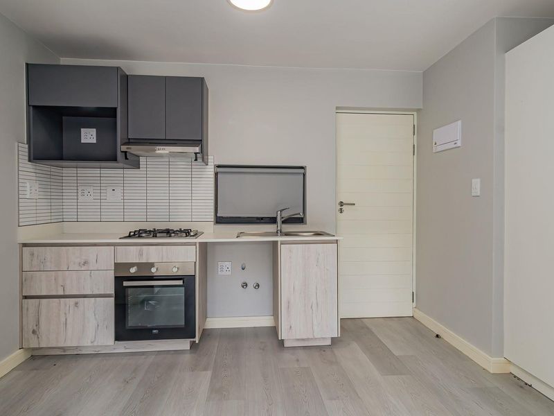 Modern kitchen featuring light wood-look cabinetry, dark overhead cupboards, built-in oven, gas cooktop, and a tiled splashback in a clean, neutral space.