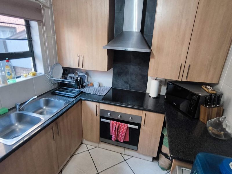 Compact kitchen featuring light wood cabinetry, granite countertops, a double sink, and integrated stainless steel appliances including an oven and extractor fan.