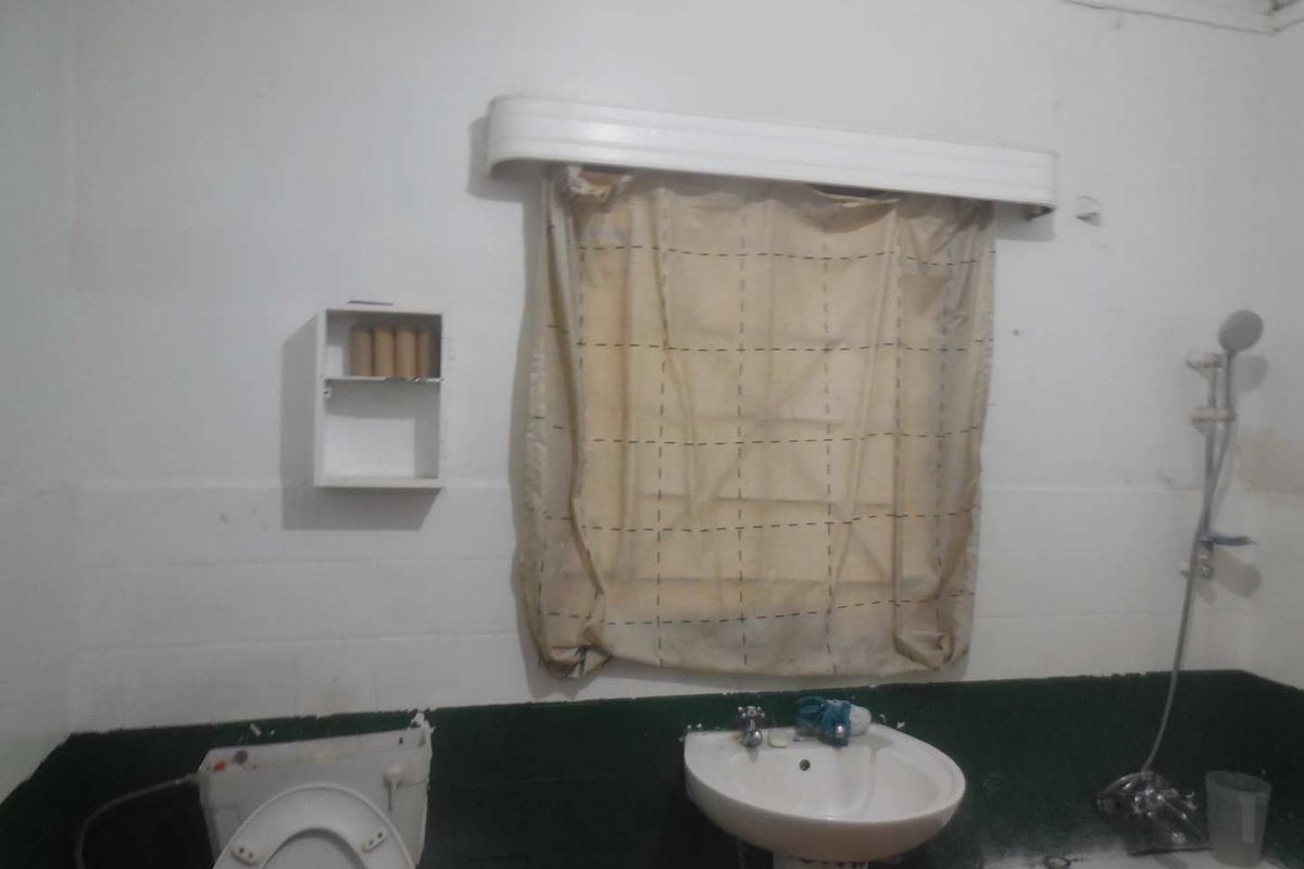 A dated bathroom featuring a pedestal basin, toilet, and shower fixture, requiring cosmetic updates and renovation to improve its overall condition.