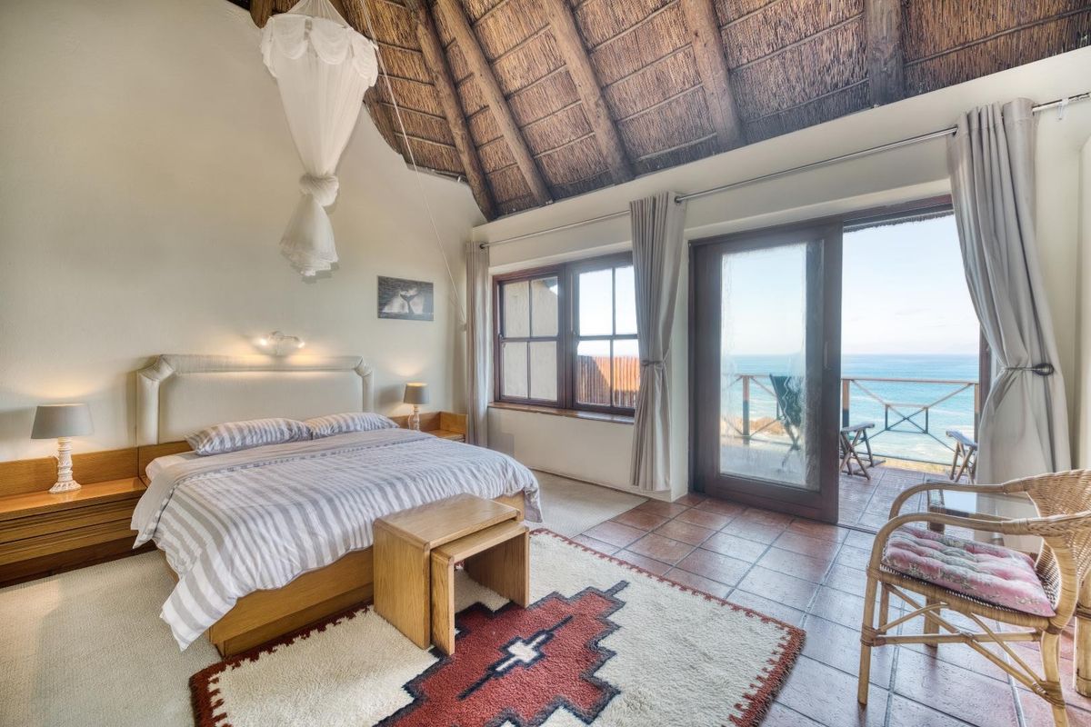 Spacious bedroom featuring a high vaulted thatched ceiling, tiled flooring, and sliding glass doors opening onto a balcony with scenic ocean views.