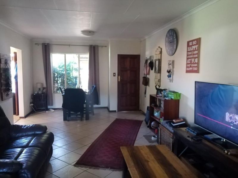 A spacious living room featuring tiled flooring, a wooden entrance door, and a sliding glass door providing natural light and access to the exterior.