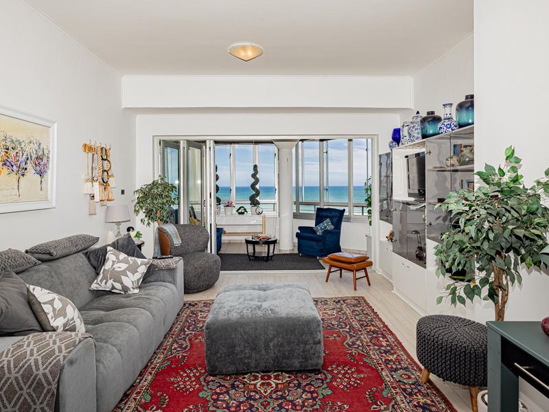 A bright living room featuring tiled flooring and large sliding glass doors that open onto a balcony with ocean views.
