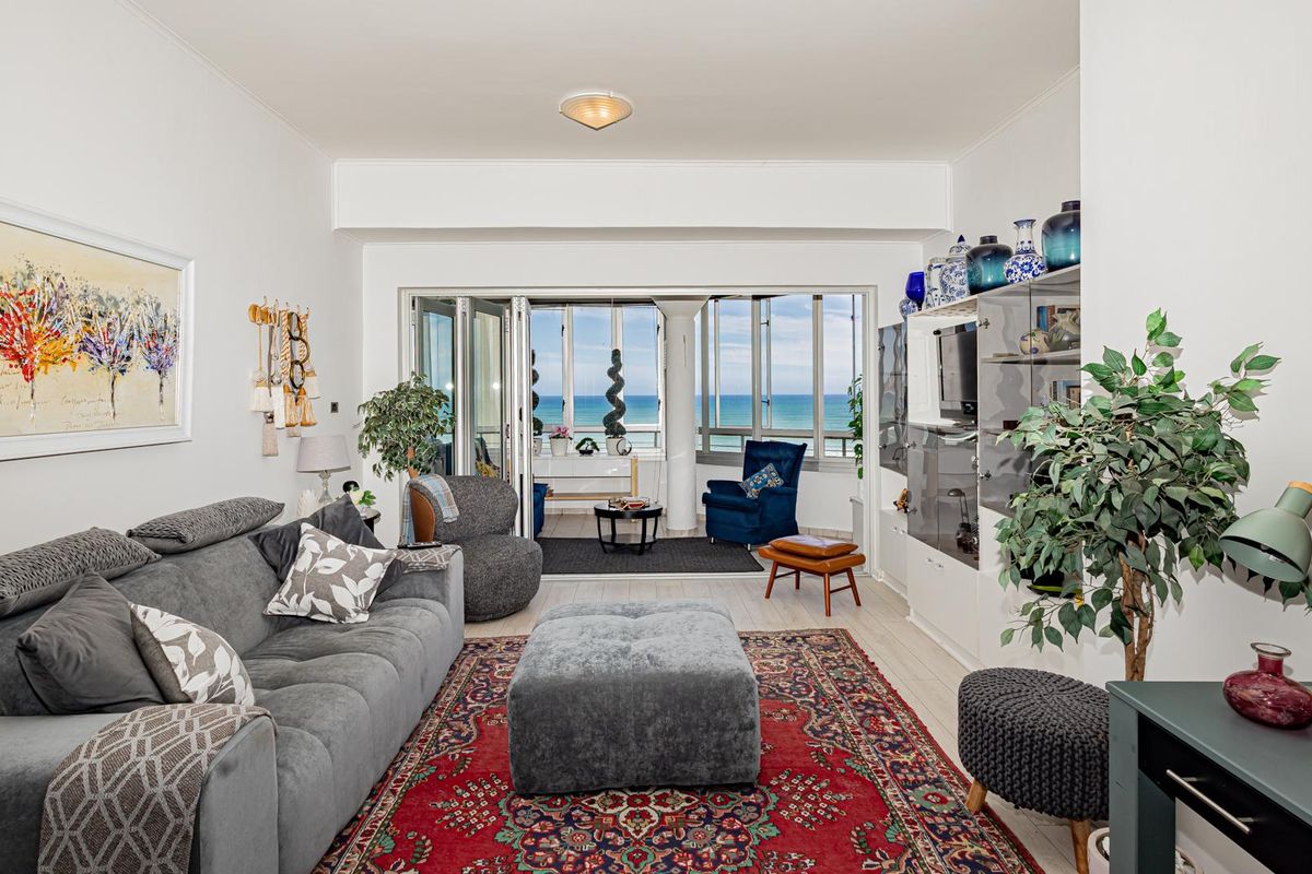 A bright living room featuring tiled flooring and large sliding glass doors that open onto a balcony with ocean views.