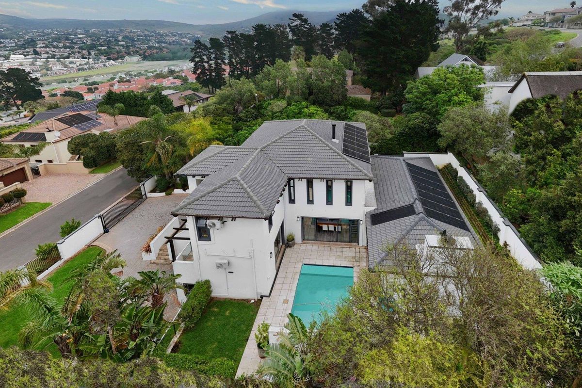 Aerial view of a residential property featuring a tiled roof with solar panels, a swimming pool, paved patio area, and landscaped garden.