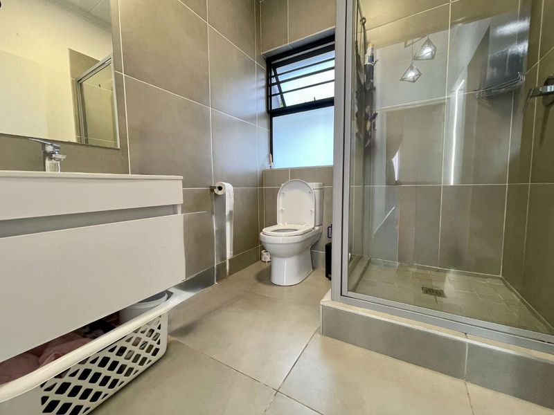 Modern bathroom featuring a vanity cabinet with basin, a glass-enclosed shower, and neutral floor-to-ceiling wall tiling.