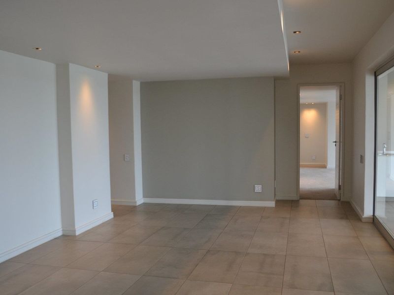 A bright, open-plan living area featuring neutral tiled flooring, recessed downlighting, and large sliding glass doors leading to an outdoor space.