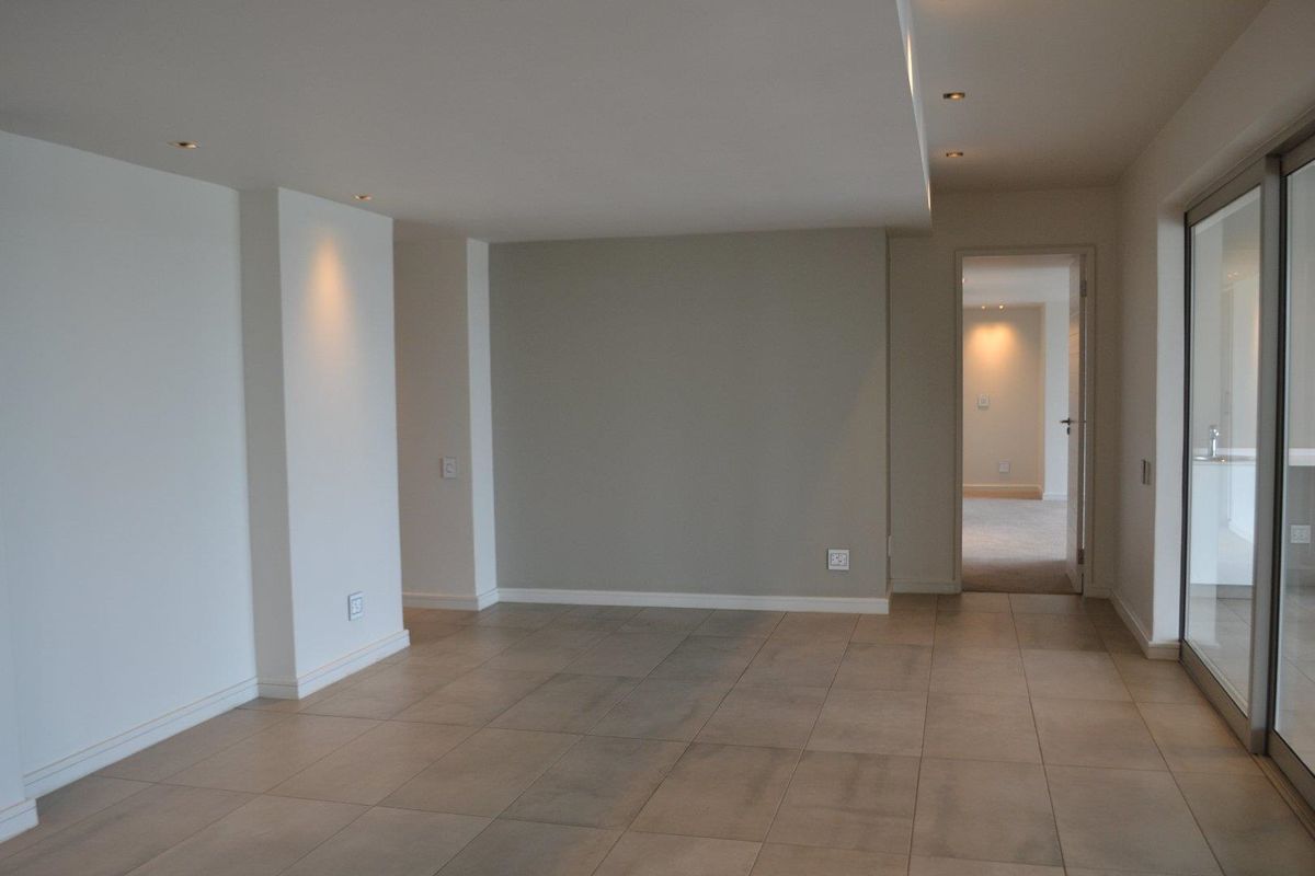 A bright, open-plan living area featuring neutral tiled flooring, recessed downlighting, and large sliding glass doors leading to an outdoor space.