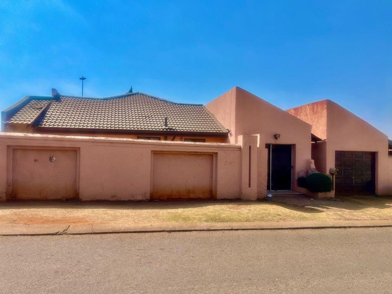 Front elevation of a residential property featuring a tiled roof, boundary wall, and garage access, showing signs of exterior wear and weathering.