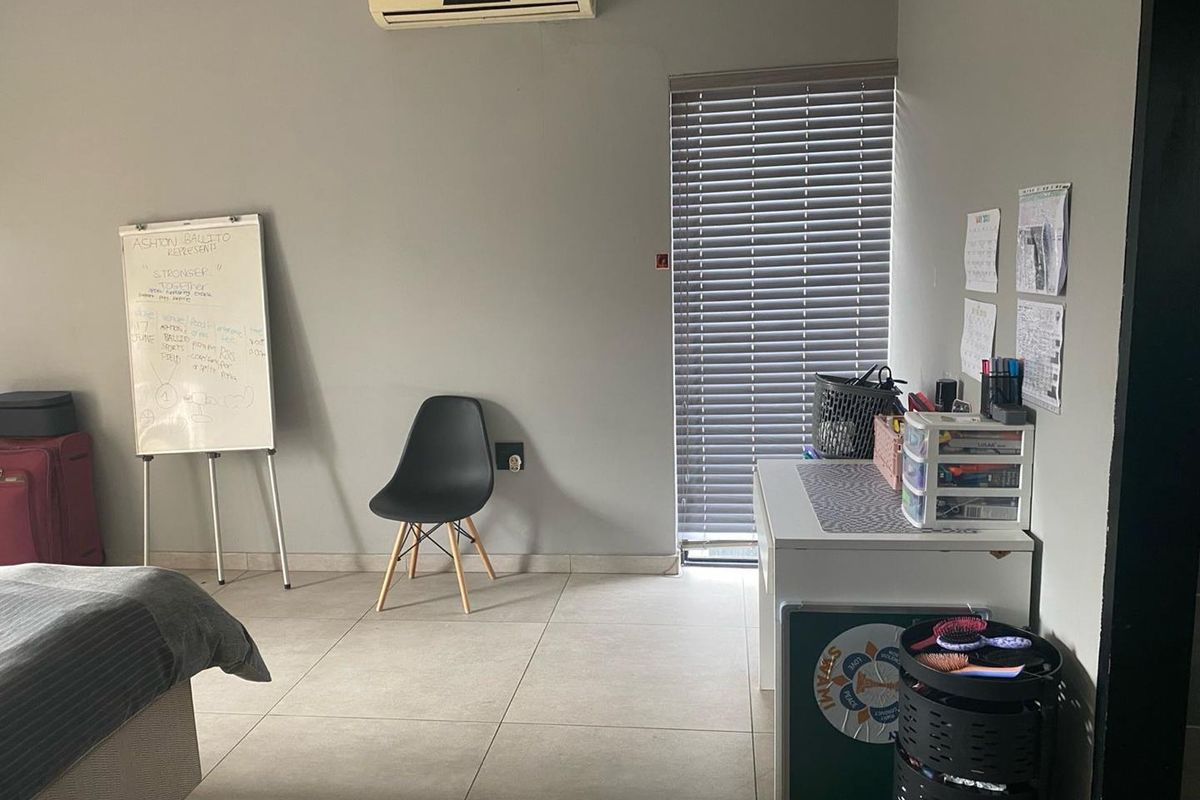 A functional bedroom space featuring tiled flooring, a wall-mounted air conditioning unit, and venetian blinds.