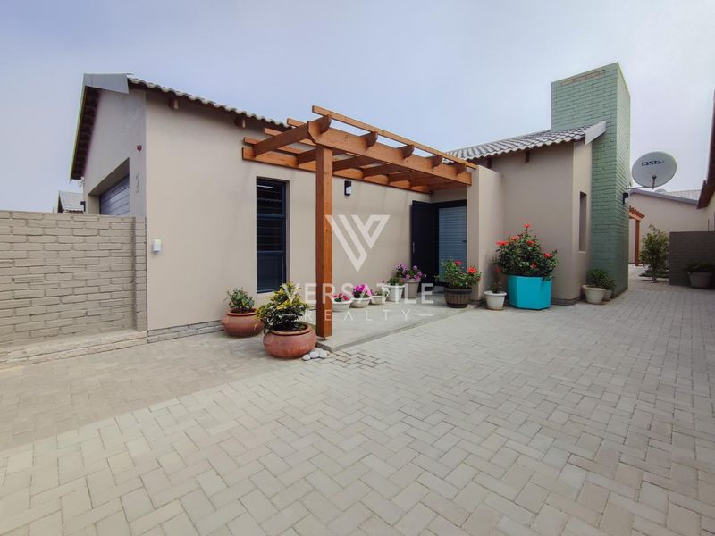 Front exterior view of a townhouse featuring a paved driveway, timber pergola entrance, and a prominent brick chimney.