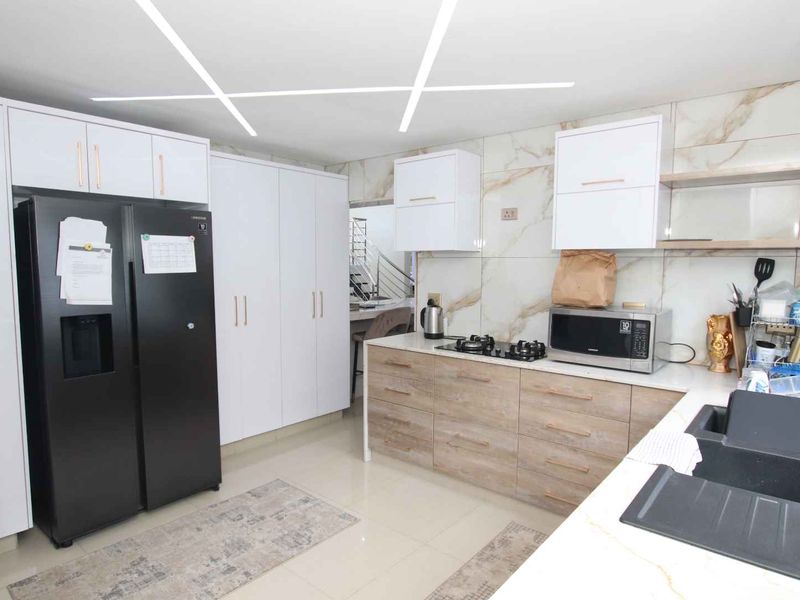 Modern kitchen featuring sleek white and wood-grain cabinetry, marble-look wall tiles, stone countertops, and contemporary linear ceiling lighting.
