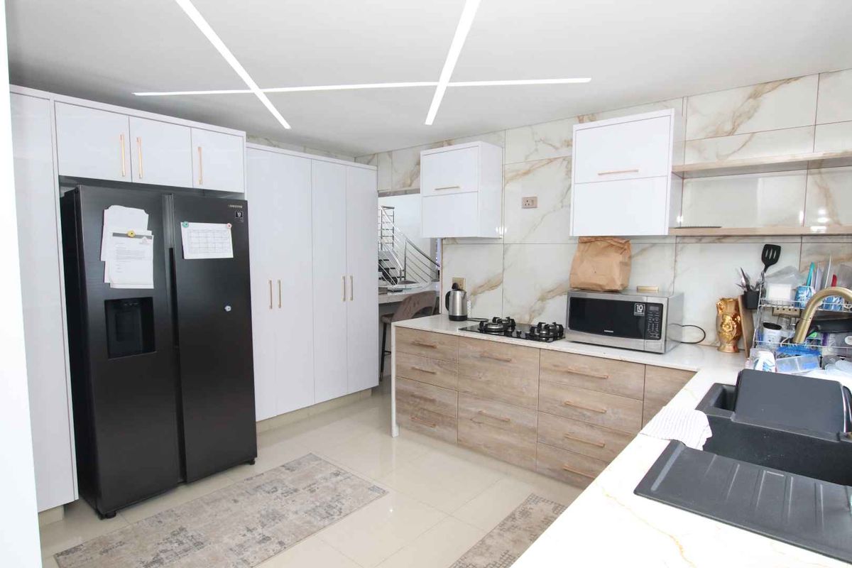 Modern kitchen featuring sleek white and wood-grain cabinetry, marble-look wall tiles, stone countertops, and contemporary linear ceiling lighting.