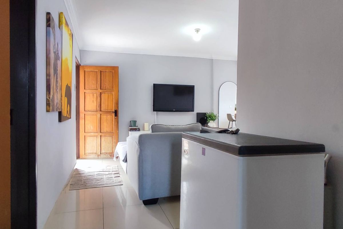 A view from a hallway into a living area featuring tiled flooring, a solid timber door, and a wall-mounted television.