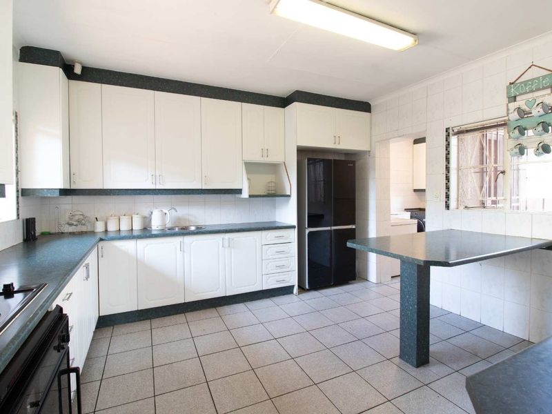 A functional kitchen featuring white cabinetry, dark laminate countertops, ceramic tile flooring, and a built-in breakfast bar with direct access to a scullery area.