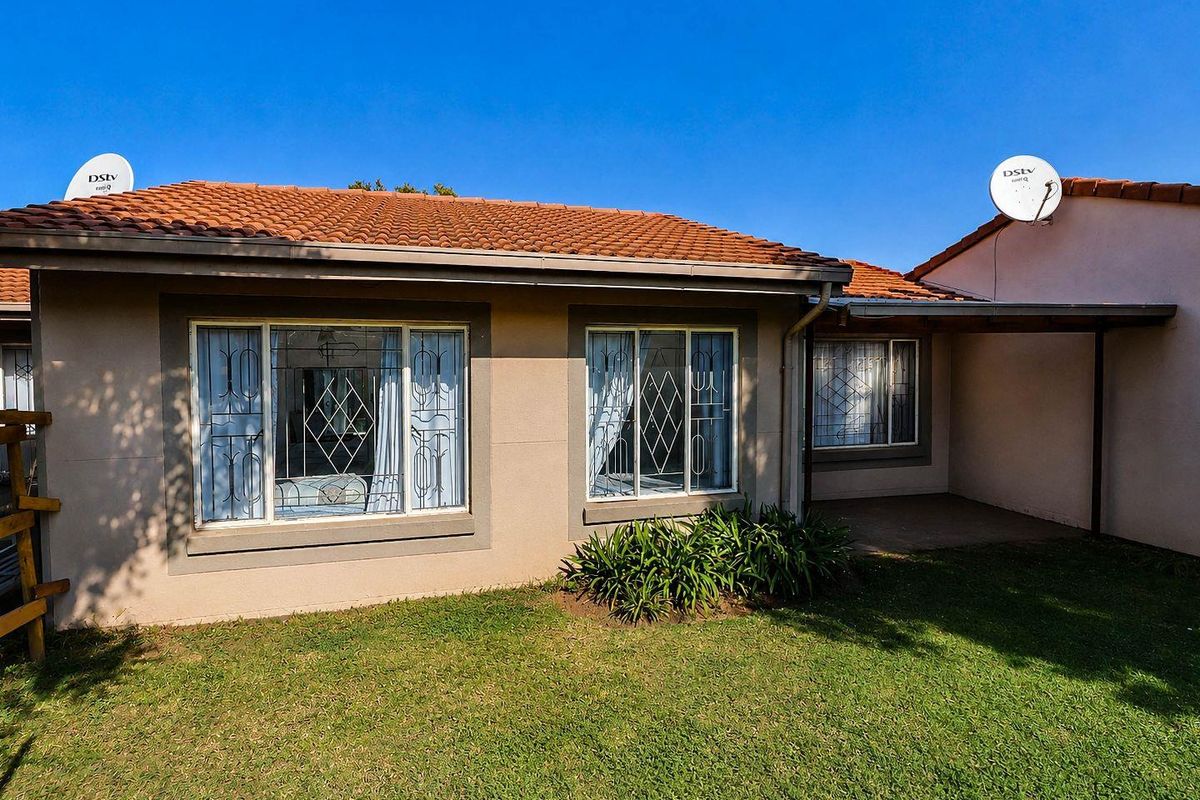 Rear view of the townhouse featuring a tiled roof, security-barred windows, and a small covered patio area overlooking the private garden.