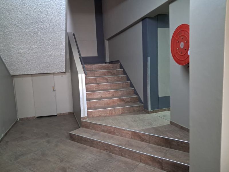 A clean, functional office building hallway featuring a tiled staircase with a metal handrail and a wall-mounted fire hose reel.