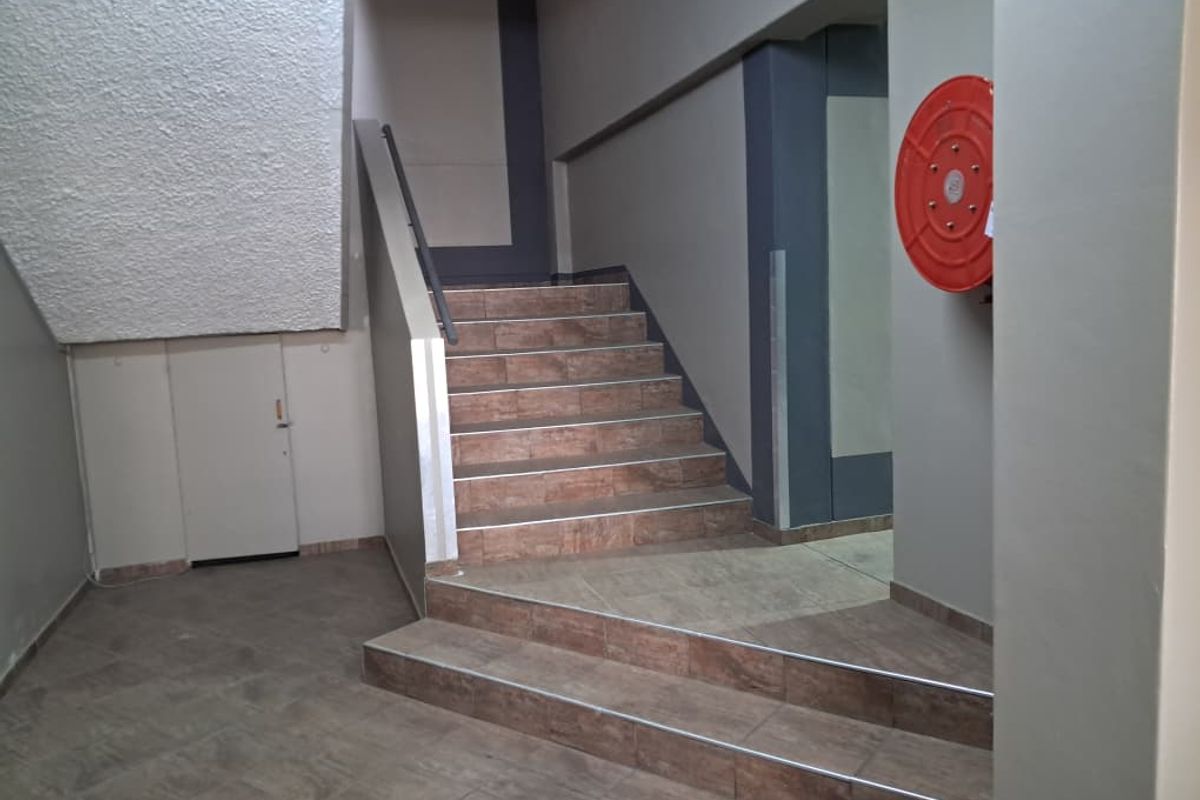 A clean, functional office building hallway featuring a tiled staircase with a metal handrail and a wall-mounted fire hose reel.