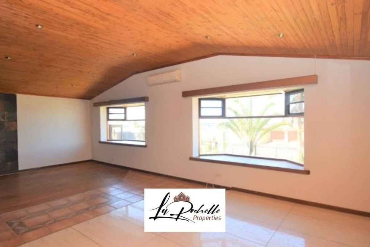 Spacious living area featuring a vaulted timber-clad ceiling, large windows, tiled flooring, and a built-in wall-mounted air conditioning unit.