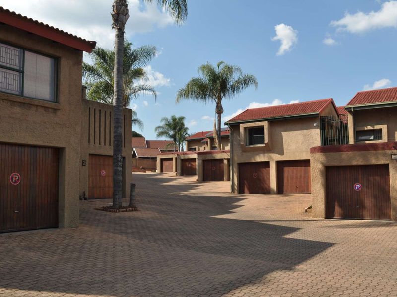 A view of the townhouse complex driveway featuring multiple garage units, paved surfaces, and established palm trees under a clear sky.