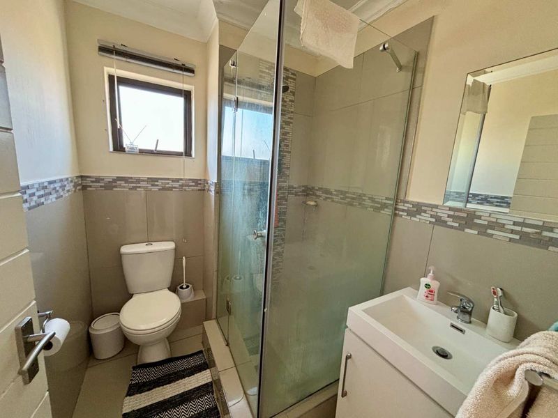 A functional bathroom featuring a glass-enclosed shower, a modern vanity with a basin, and neutral wall tiling.