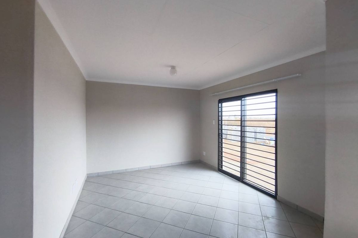 A bright, empty bedroom featuring neutral wall paint, tiled flooring, and a sliding glass door with security bars.