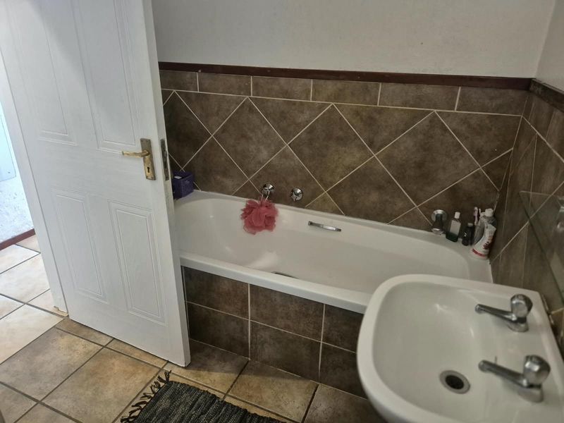 A functional bathroom featuring a built-in bathtub with tiled surround and a wall-mounted basin with chrome fixtures.