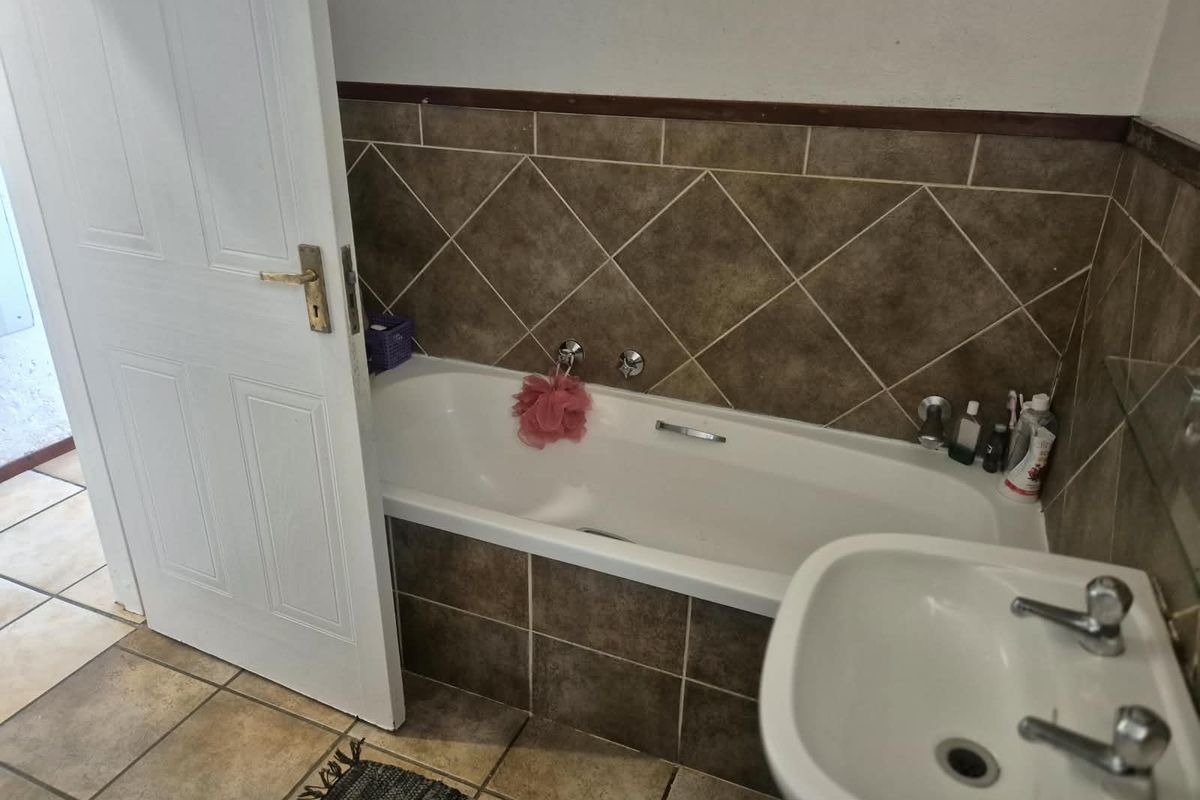 A functional bathroom featuring a built-in bathtub with tiled surround and a wall-mounted basin with chrome fixtures.