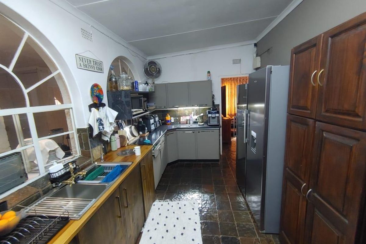 A functional kitchen featuring wooden cabinetry, tiled flooring, and a distinctive arched window, offering a practical layout with ample storage space.