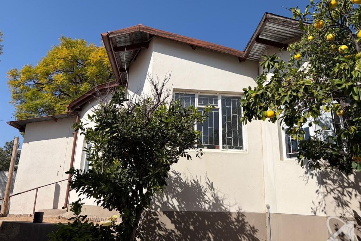 A view of the rear exterior elevation of the house, featuring plastered walls, metal roofing, and security-fitted windows.