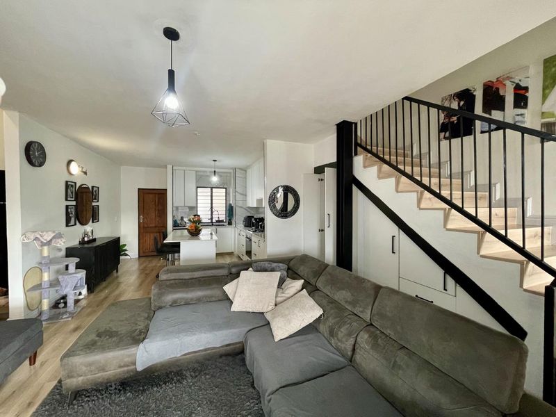 Open-plan living area featuring a modern kitchen with island, laminate flooring, and a staircase with integrated under-stair storage and metal balustrade.