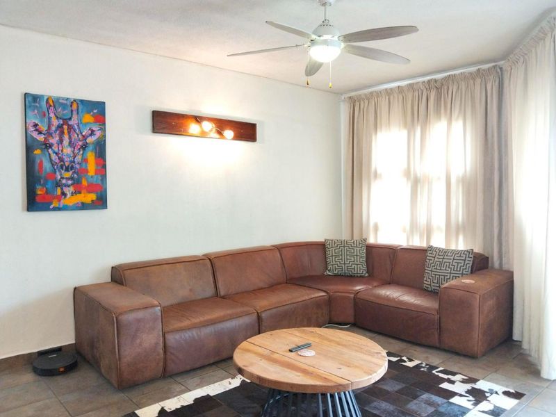 A comfortable living room featuring tiled flooring, a ceiling fan, and wall-mounted lighting, creating a functional and inviting space.