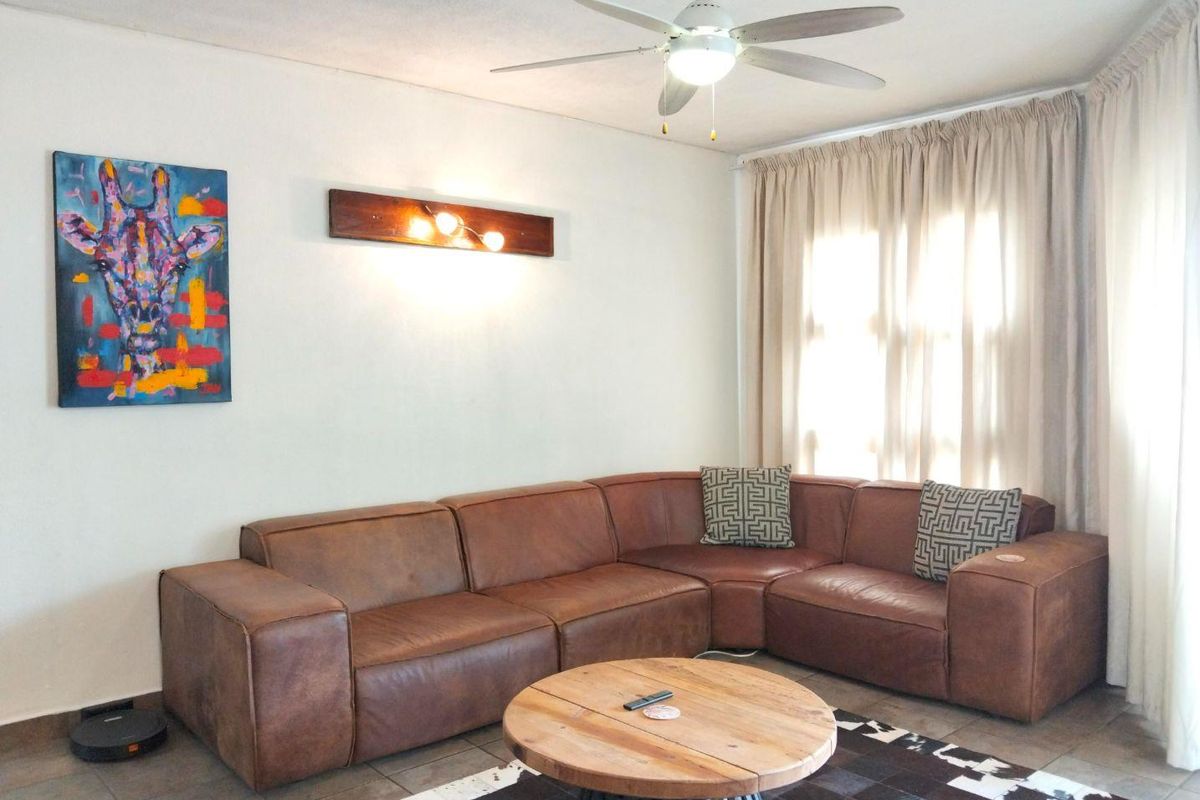 A comfortable living room featuring tiled flooring, a ceiling fan, and wall-mounted lighting, creating a functional and inviting space.