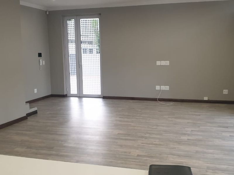 Spacious, empty living area featuring modern laminate flooring, neutral wall tones, and large sliding glass doors providing access to the outdoor space.
