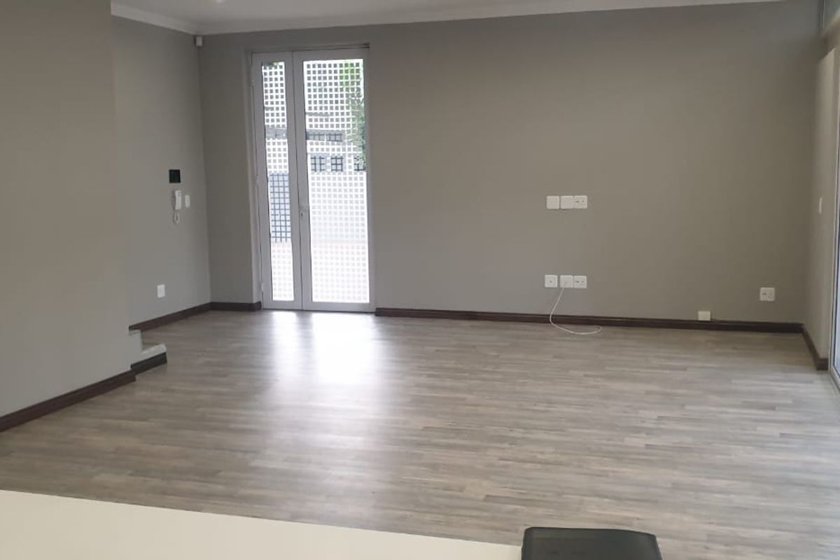 Spacious, empty living area featuring modern laminate flooring, neutral wall tones, and large sliding glass doors providing access to the outdoor space.