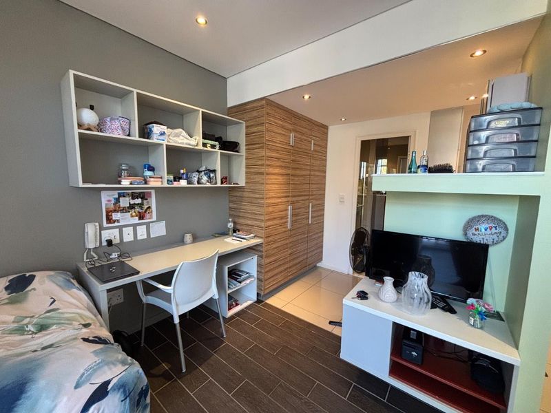A functional bedroom featuring built-in cabinetry, a dedicated desk area with shelving, recessed lighting, and tiled flooring throughout.
