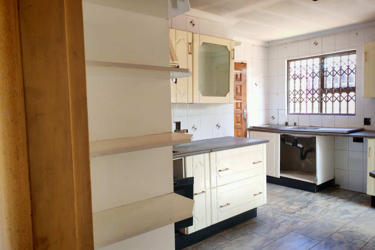 A dated kitchen featuring built-in cabinetry, tiled walls, and a window with security bars. The space requires renovation and modernization of fixed finishes.