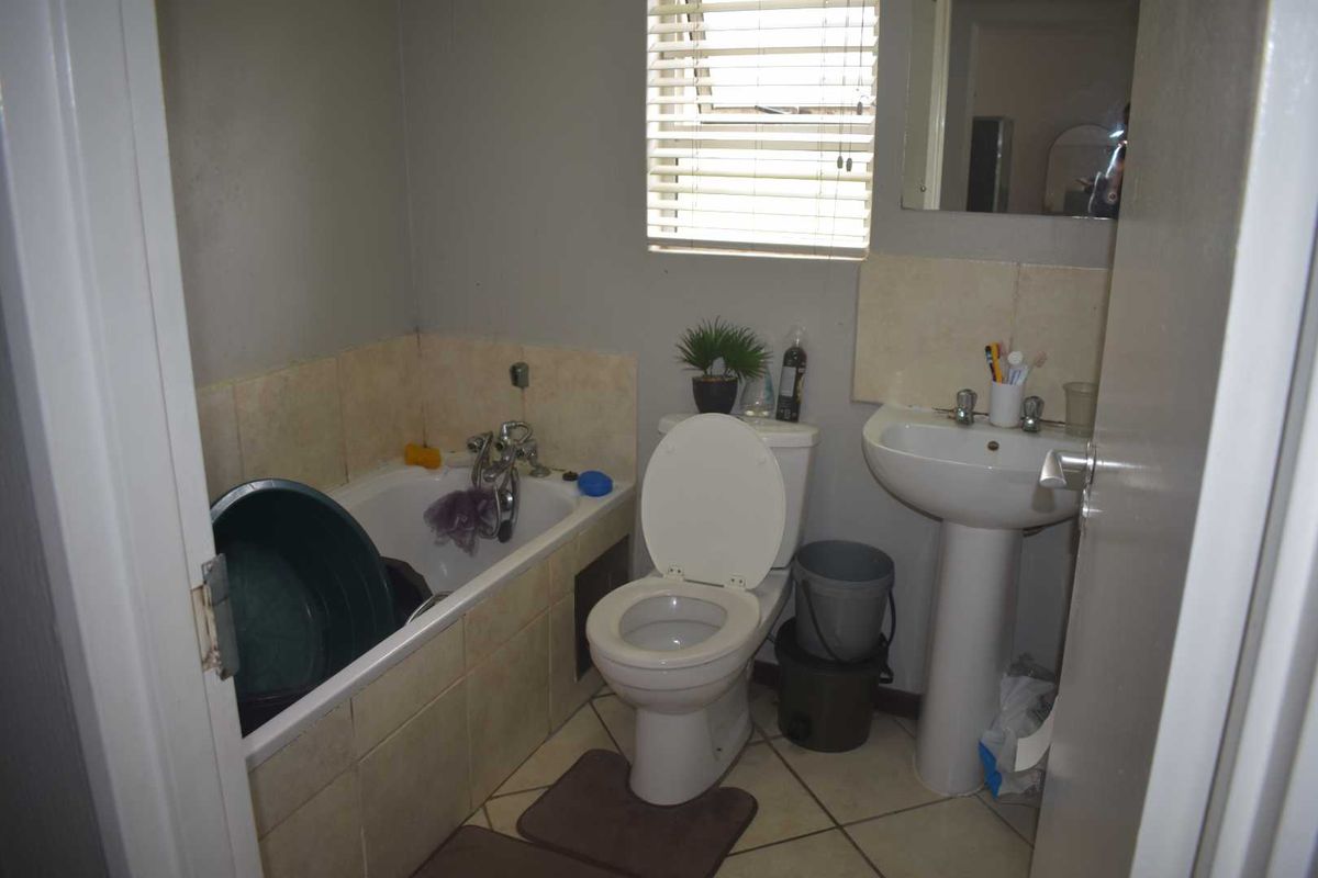 A functional bathroom featuring a bathtub with shower mixer, pedestal basin, and toilet, finished with neutral wall and floor tiling.