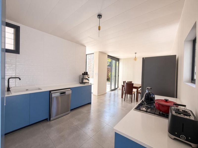 Modern open-plan kitchen and dining area featuring blue cabinetry, white countertops, gas hob, and direct access to the outdoor space through sliding doors.
