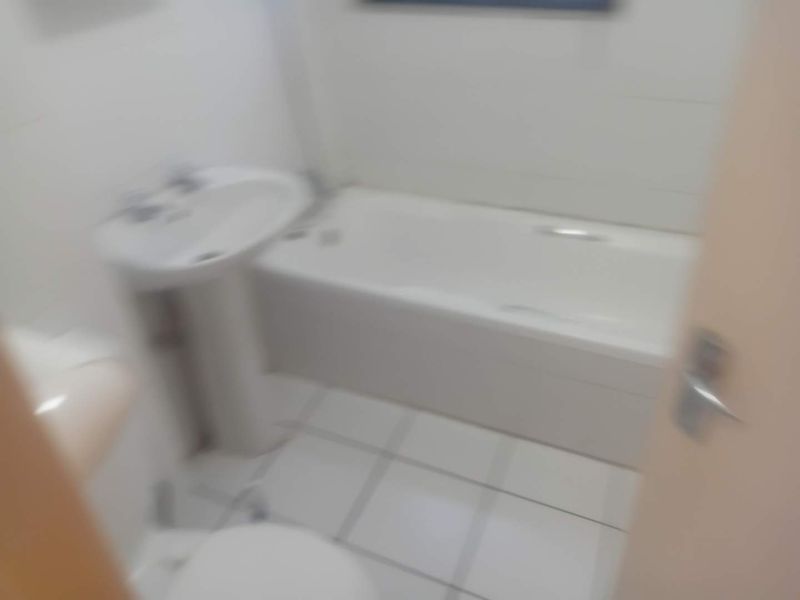 A functional bathroom featuring a pedestal basin, bathtub, and toilet with tiled finishes.